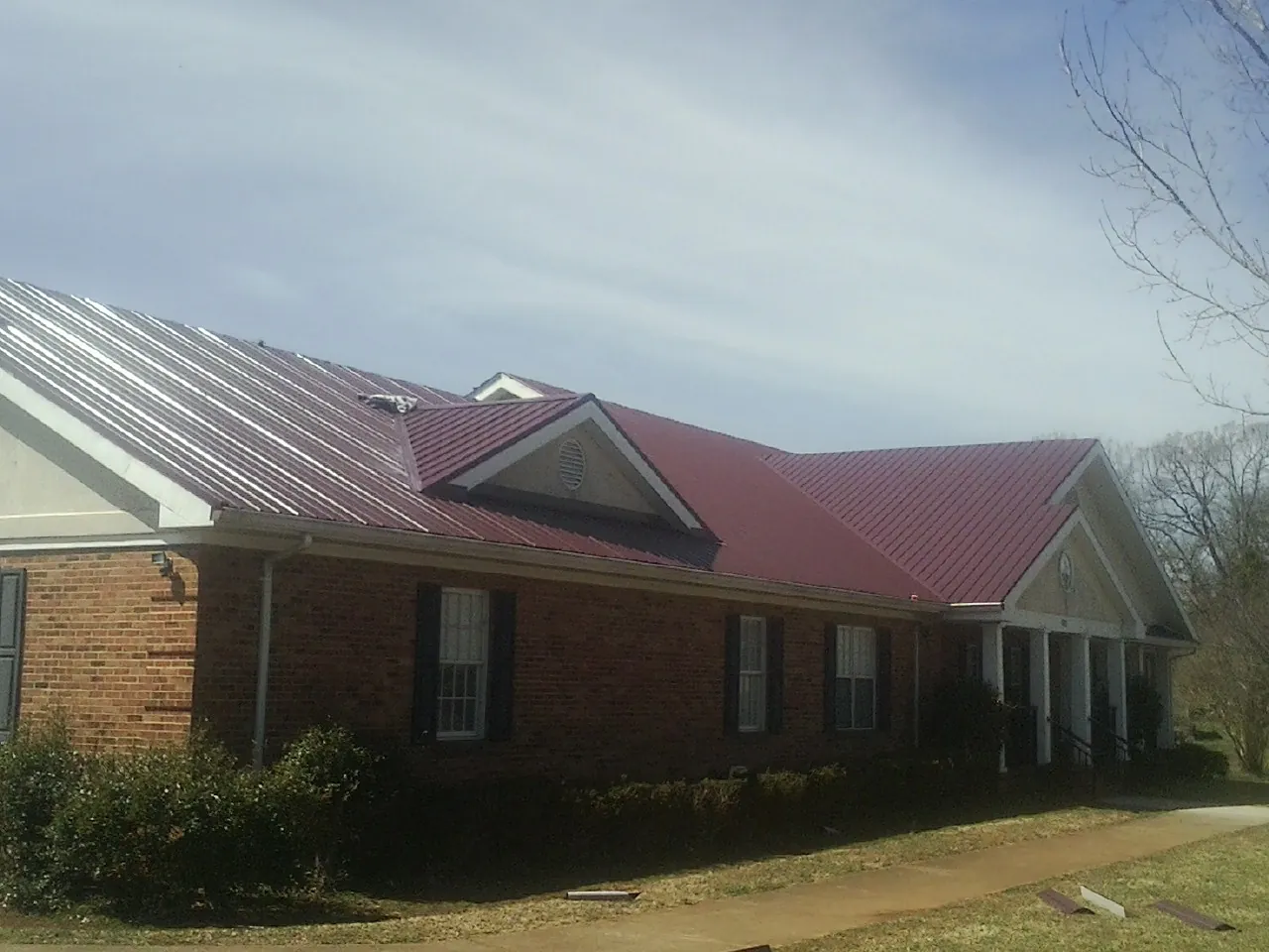 Red metal roof with gabled entries on a long brick building, from a Hail Damage Roof Repair job in Scituate