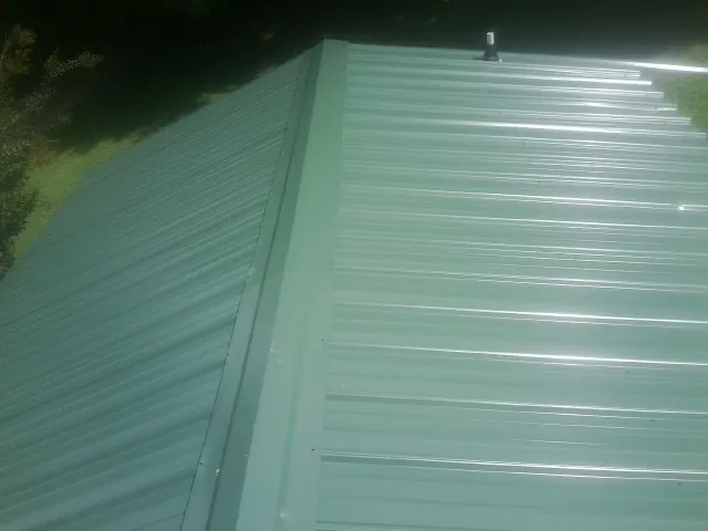 New green metal panels meeting at the ridge of a roof — Flat Roof Repair work by our crew in Scituate