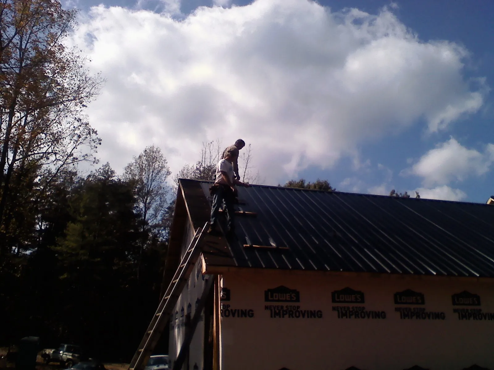 Roofer fastening dark metal panels high against a cloudy sky, from a Roof Inspection job in Scituate