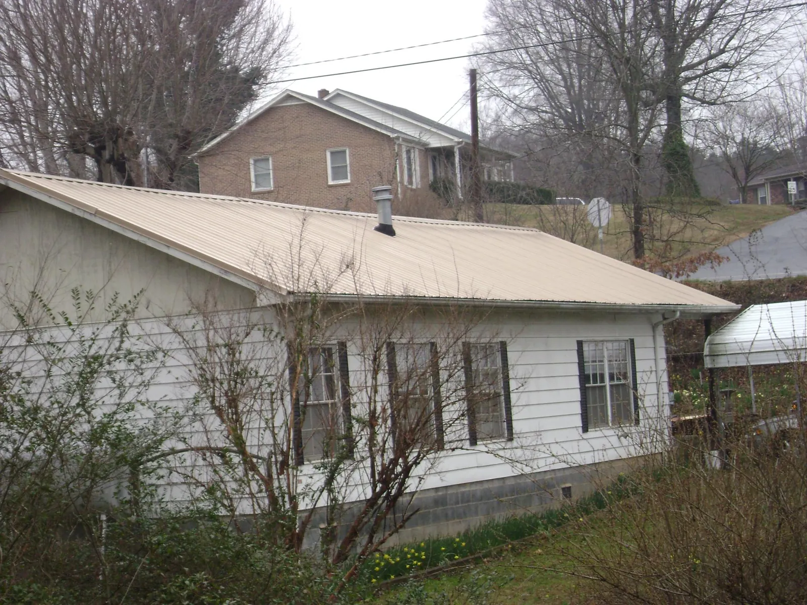 Tan metal roof on a white sided house set into a hillside — Commercial Roofing by Roofing Brothers in Scituate