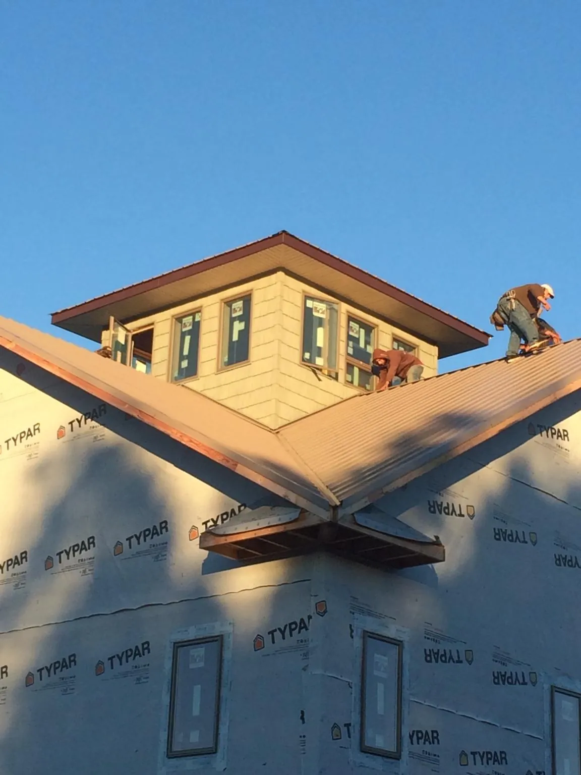 Roofers working around a rooftop cupola on a new metal roof at sunset — Roof Waterproofing in Scituate by Roofing Brothers